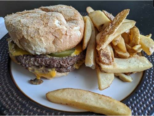 A juicy cheeseburger with pickles and mushrooms, served with golden French fries on a white plate.