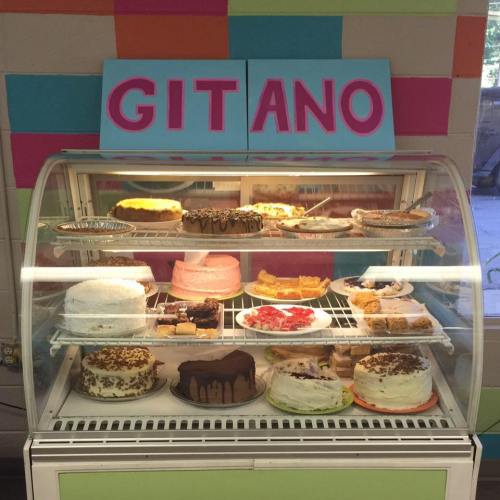 Display case filled with various cakes and desserts, labeled "GITANO" above. Colorful and inviting treats.