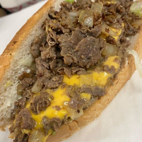 Close-up of a cheesesteak sandwich filled with sautéed beef, melted cheese, and onions on a soft hoagie roll.