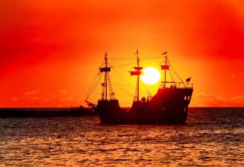 Silhouette of a ship against a vibrant orange sunset over the ocean.