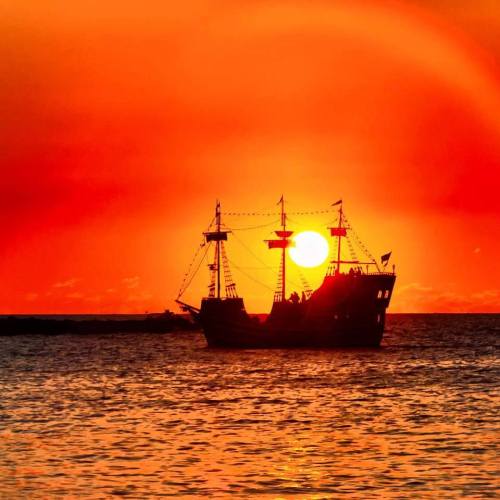 Silhouette of a ship against a vibrant orange sunset over the ocean.