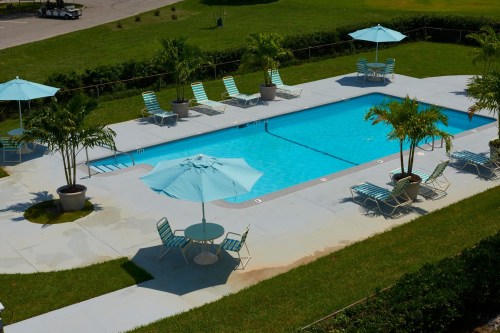 Aerial view of a pool surrounded by lounge chairs and umbrellas, set in a green, landscaped area.