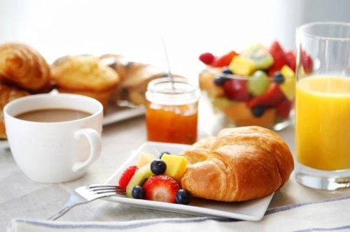 A breakfast spread featuring a croissant, fresh fruit, coffee, orange juice, and a jar of jam on a table.