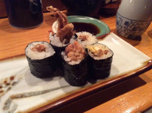 A plate of sushi rolls with crispy toppings, served with soy sauce on a wooden table.