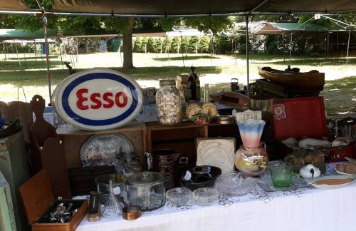 A display of vintage items and antiques, including glassware, a large Esso sign, and various collectibles under a tent.