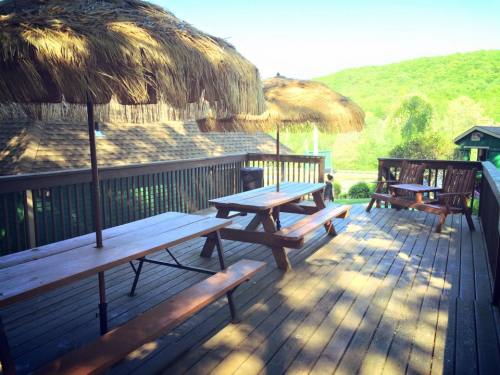 A wooden deck with picnic tables and thatched umbrellas, surrounded by green hills and trees.