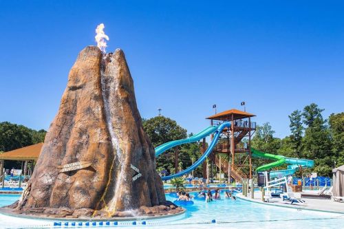 A water park featuring a large volcano structure with flames, surrounded by a pool and water slides in the background.