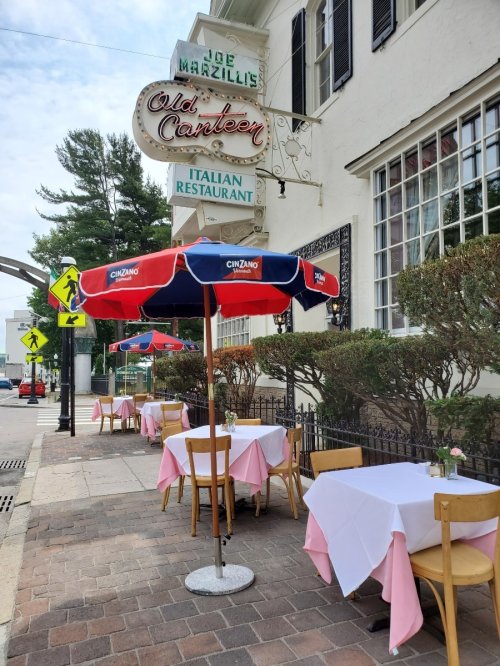 Outdoor dining area of an Italian restaurant with tables set under umbrellas, featuring pink tablecloths and a vintage sign.