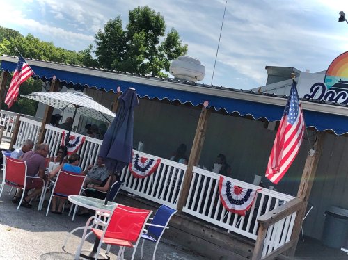 Outdoor dining area with American flags and festive decorations, patrons seated under umbrellas on a sunny day.