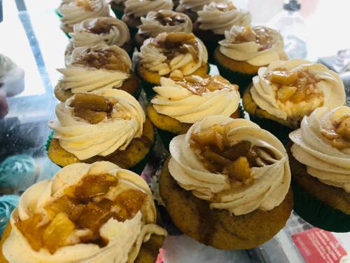 A close-up of cupcakes topped with swirls of frosting and apple pie filling, arranged neatly on a display.