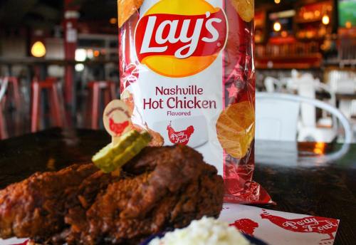 A plate with fried chicken, pickles, and rice, alongside a bag of Lay's Nashville Hot Chicken flavored chips.