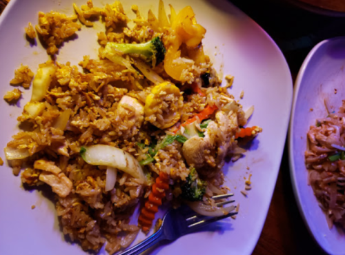 A plate of fried rice with vegetables and chicken, garnished with colorful peppers and a fork on the side.