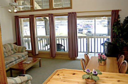 Cozy living area with a sofa, dining table, and large windows overlooking a marina. Potted plants add a touch of greenery.