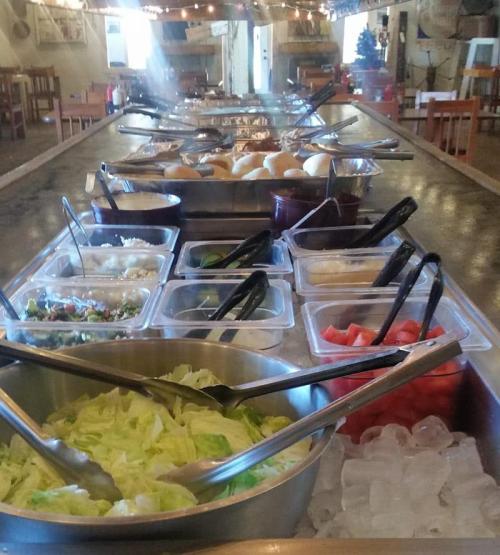 A long table set with various food items, including salads, toppings, and bread rolls, in a rustic dining area.