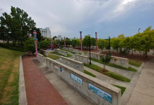 A park with colorful light poles, concrete pathways, and greenery under a cloudy sky.