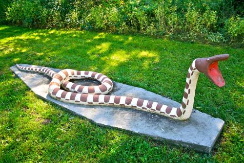 A large, colorful snake sculpture with a red mouth and patterned body, resting on a stone base in a grassy area.