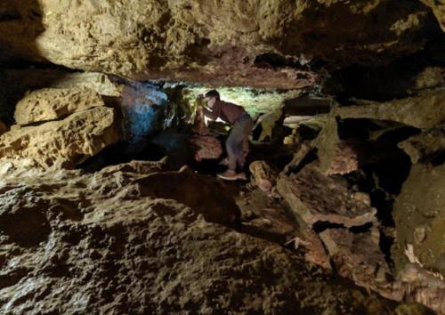 A person exploring a rocky cave, illuminated by soft light, surrounded by uneven terrain and natural formations.