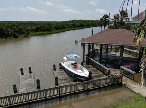 A boat docked at a wooden pier beside a calm waterway, surrounded by lush greenery and a clear sky.