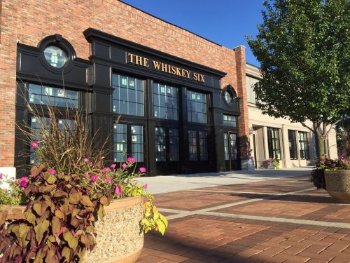Exterior of "The Whiskey Six" building with large windows, brick facade, and colorful flower planters in front.