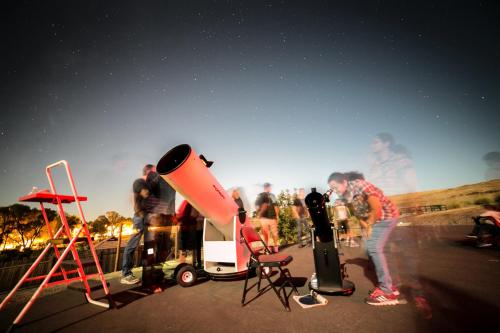 A night scene with people observing stars through telescopes, with a clear sky filled with stars in the background.