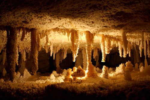 A dimly lit cave with stunning stalactites and stalagmites, illuminated by a warm glow.