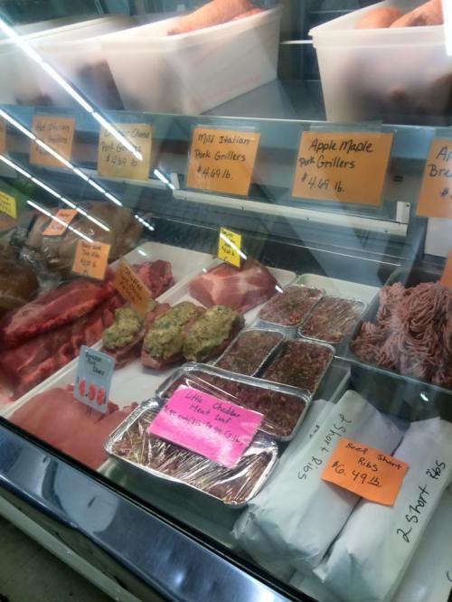 A display case filled with various meats, including pork, beef, and sausages, with price tags visible.