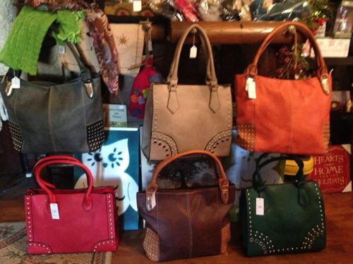 A display of various handbags in different colors and styles, featuring studded designs and tags for pricing.