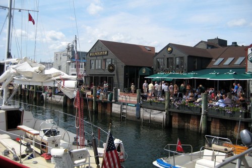 A bustling waterfront scene with boats, restaurants, and people enjoying a sunny day by the water.