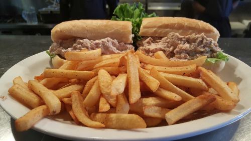 A plate with two sandwiches filled with tuna salad and lettuce, accompanied by a side of golden French fries.
