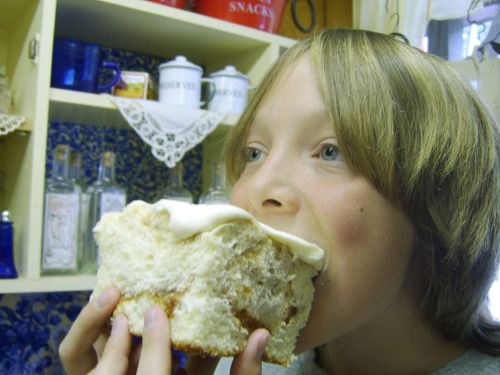 A young boy takes a big bite of a large piece of cake in a cozy kitchen setting.