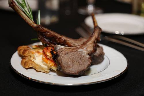 A plate with two lamb chops garnished with rosemary, served alongside a slice of savory pie.