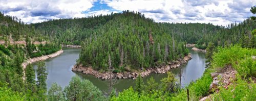A panoramic view of a winding river surrounded by lush green forests and cloudy skies.