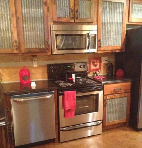 A modern kitchen featuring stainless steel appliances, wooden cabinets, and a black countertop with a red towel hanging.