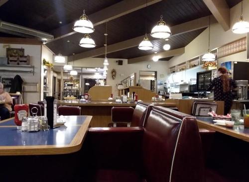 A cozy diner interior with red booths, a blue table, and warm lighting, featuring a counter and kitchen in the background.