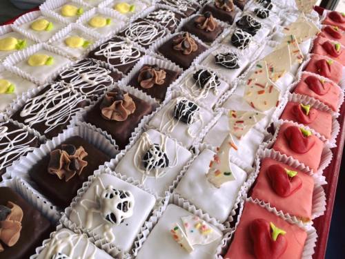 A colorful assortment of small, decorated pastries arranged in rows, featuring various toppings and designs.