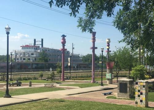 Colorful sculptures in a park with a riverboat in the background and green grass under a clear blue sky.