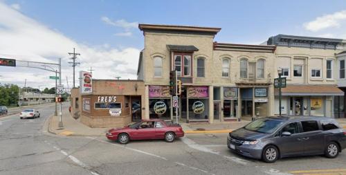 A street corner featuring a brick building with shops, traffic lights, and cars on a cloudy day.