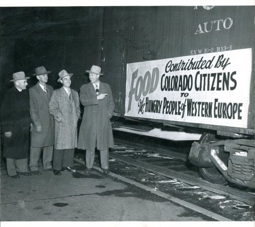 Four men in hats stand beside a train car with a sign reading "Food Contributed by Colorado Citizens to the Hungry People of Western Europe."