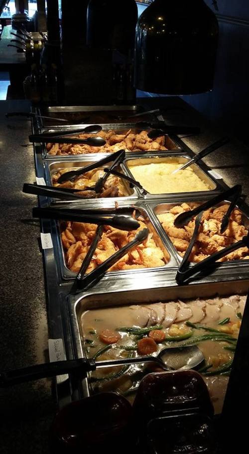 A buffet spread featuring various dishes, including fried chicken, rice, and vegetables, with serving tongs.