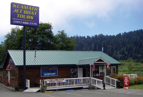 A wooden building with a green roof, sign for Klamath Jet Boat Tours, surrounded by trees and flags.
