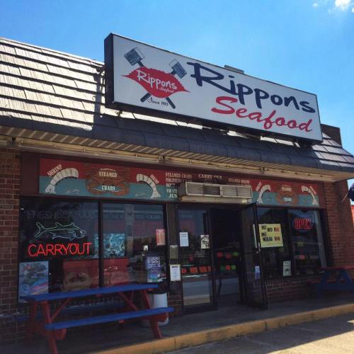 Exterior of Rippon's Seafood shop with a sign, colorful windows, and outdoor seating. "Carryout" sign visible.
