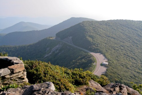 A scenic view of rolling green mountains and a winding road under a hazy sky.