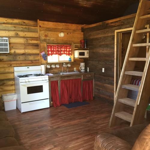 Cozy wooden cabin interior with a kitchen, stove, and a loft ladder, featuring rustic decor and warm lighting.