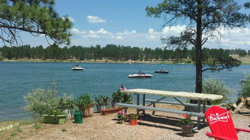A serene lakeside scene with boats on the water, surrounded by trees and colorful flower pots near a picnic table.