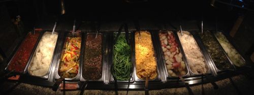 A buffet with various food trays, including mashed potatoes, green beans, rice, and mixed vegetables.