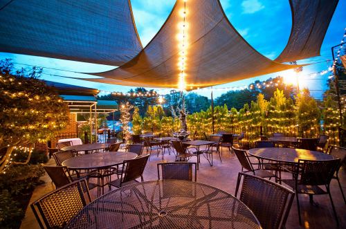 Outdoor dining area with string lights and shaded tables, surrounded by greenery at dusk.