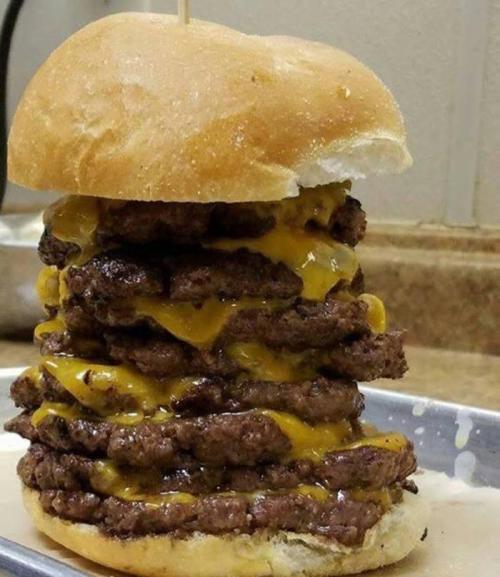 A towering burger stacked with multiple beef patties and melted cheese, resting on a bun.