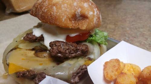 A juicy burger with melted cheese, lettuce, tomato, and onions, served with a side of crispy potato bites.