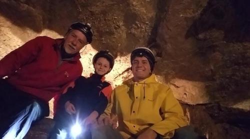 Three people in helmets pose in a cave, with one holding a flashlight, surrounded by rocky walls.