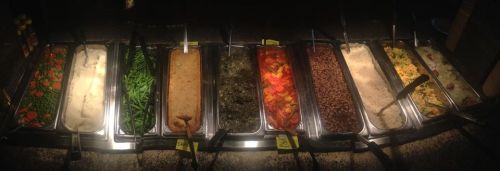 A buffet with various dishes including green beans, mashed potatoes, vegetables, and sauces in metal trays.
